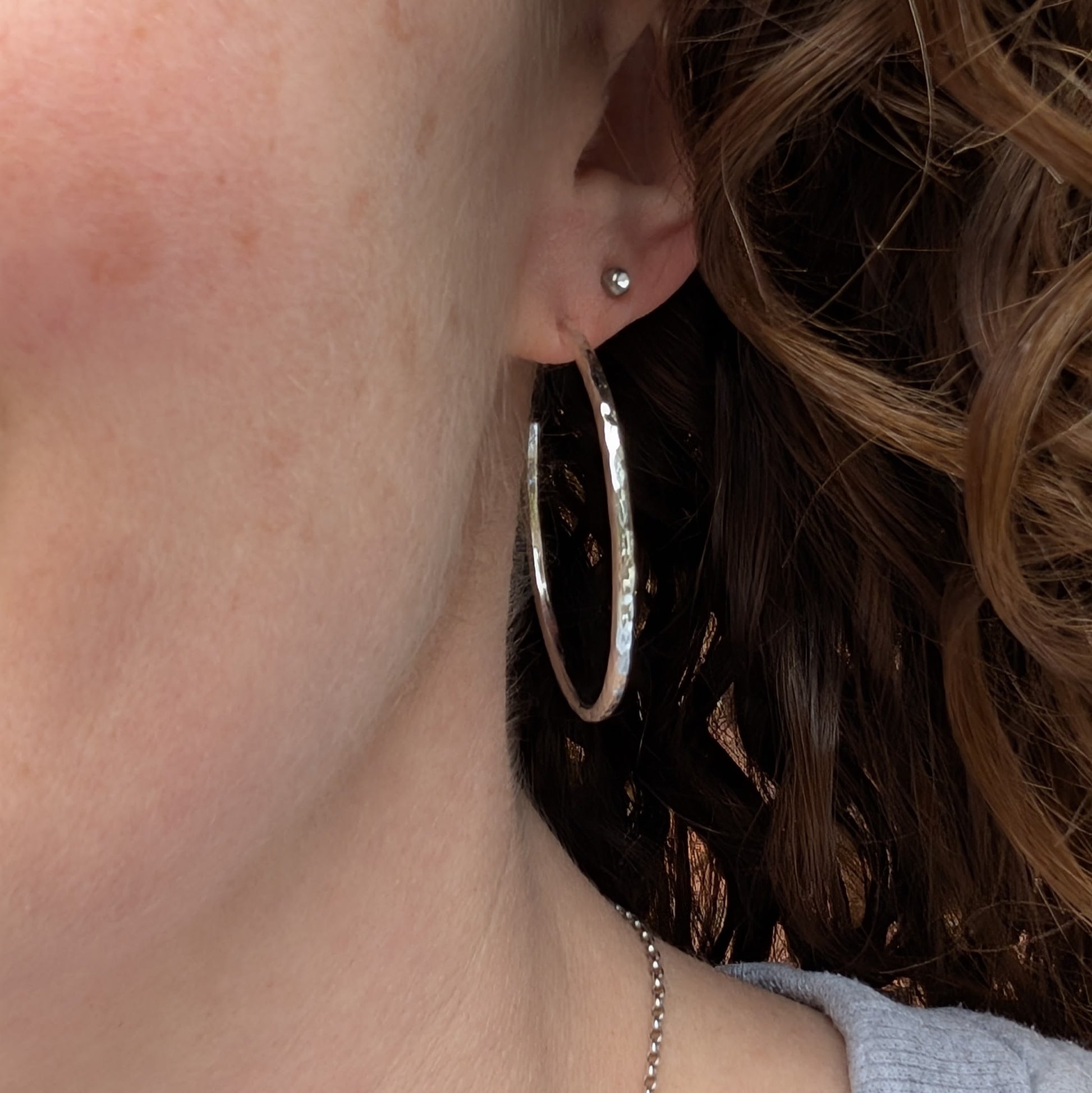 Close-up of a person wearing one of the large hammered silver hoop earrings, showing its size and reflective finish.