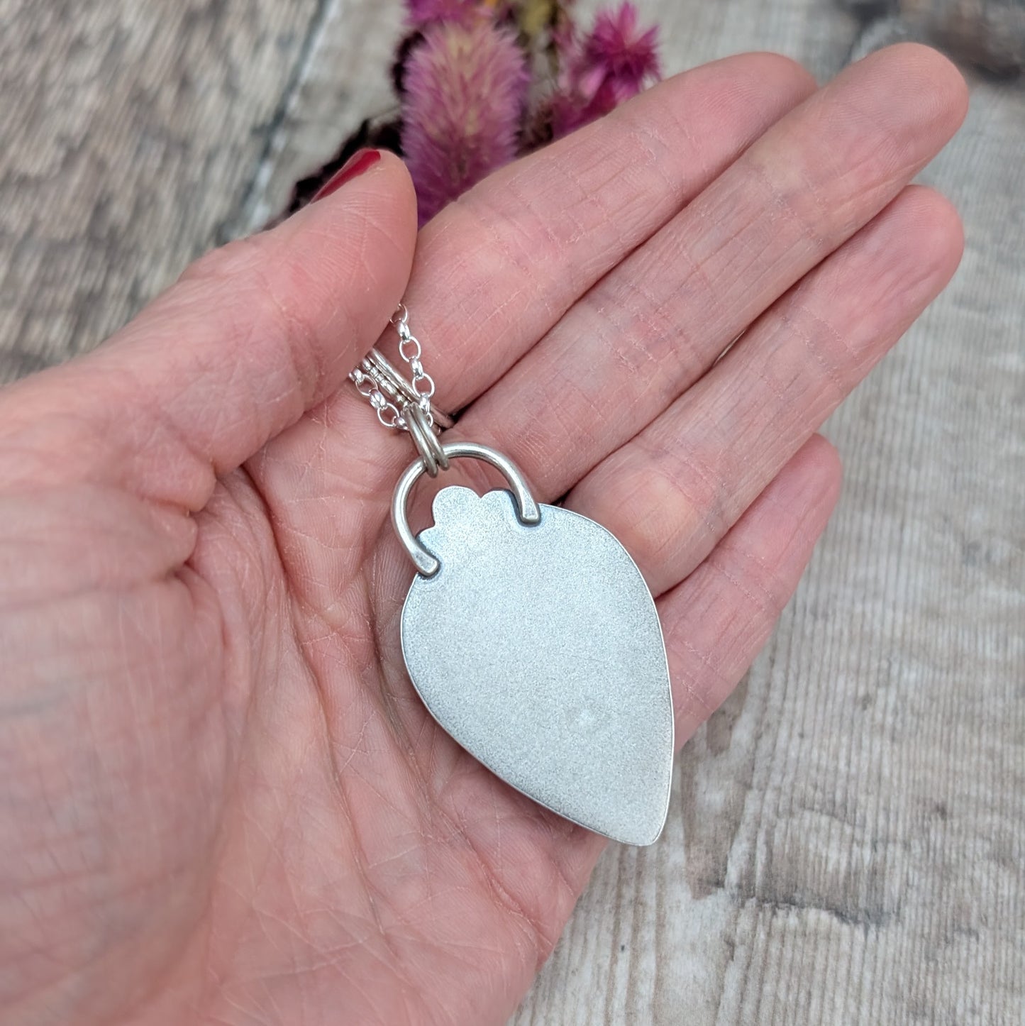 The back of the teardrop-shaped labradorite pendant, showing its smooth, matte silver finish. The pendant is attached to a sterling silver chain with a handmade silver bail.