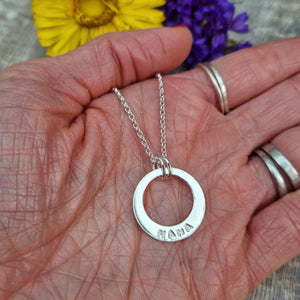 Sterling Silver ‘MAMA’ necklace. Silver disc with offset hole in centre, looks like a thick circle. Attached via two small silver hoops to silver chain. On thicker part of disc, inscription wording hammered into the silver reads MAMA in capitals. Disc measures approximately 20 mm in diameter. Chain length 18 inches.