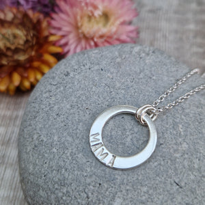 Sterling Silver ‘MAMA’ necklace. Silver disc with offset hole in centre, looks like a thick circle. Attached via two small silver hoops to silver chain. On thicker part of disc, inscription wording hammered into the silver reads MAMA in capitals. Disc measures approximately 20 mm in diameter. Chain length 18 inches.