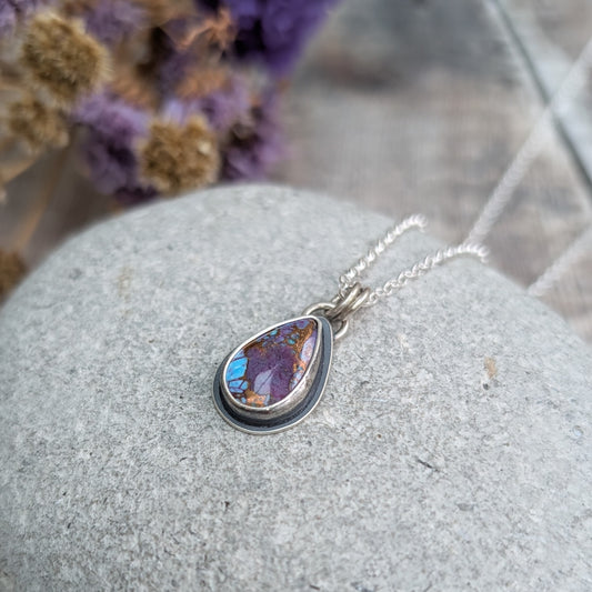 Close-up of the Mohave Turquoise necklace on a stone
Handmade recycled sterling silver necklace featuring a teardrop-shaped Mohave Turquoise stone with vibrant purple, blue, and copper tones. The oxidised silver setting contrasts with the bright silver chain, creating a unique, artisan jewellery piece.