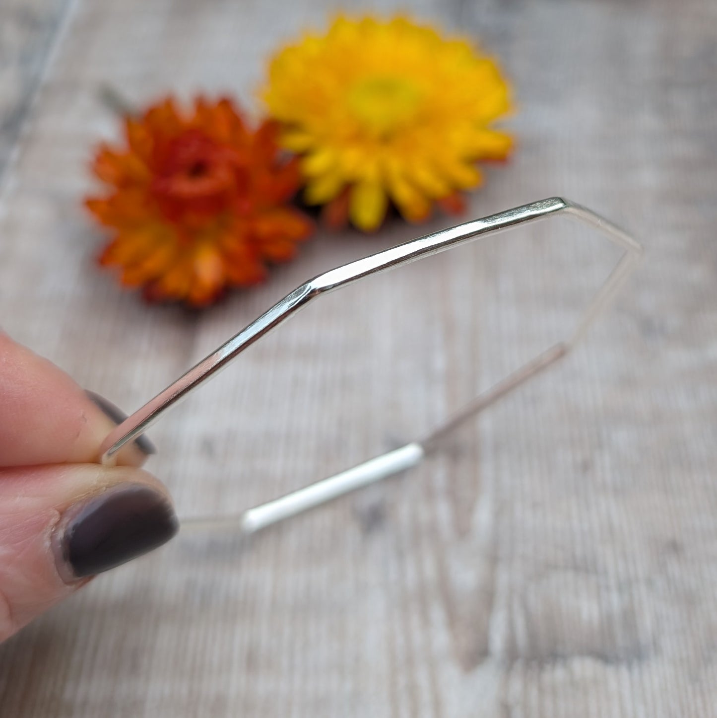 A close-up of the silver octagon bangle held between fingers, highlighting the smooth, angular design and polished finish.