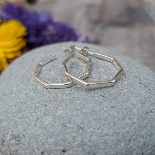 Pair of octagon hoop earrings displayed on a stone, highlighting their reflective surfaces and minimalist design with natural elements in the background.