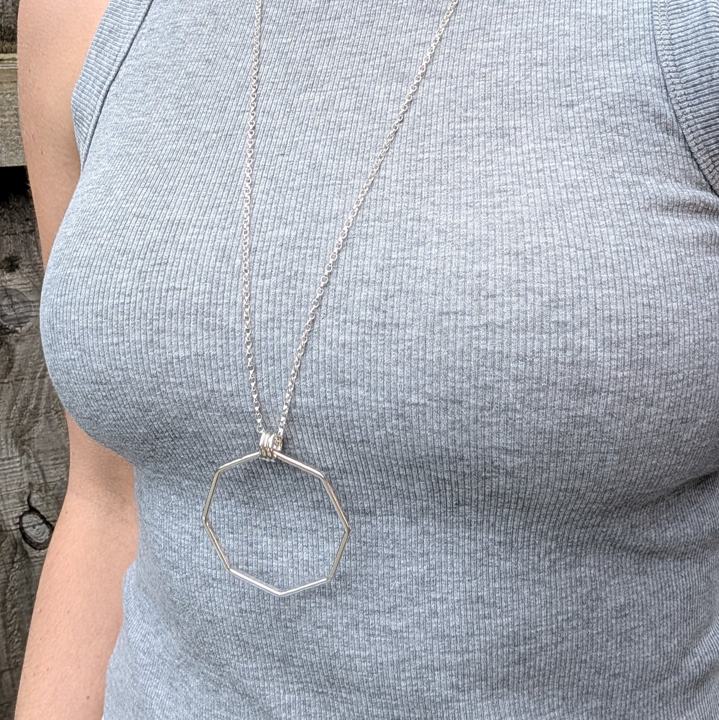A model wearing a long sterling silver octagonal pendant necklace with three polished rings, shown against a fitted grey ribbed top.