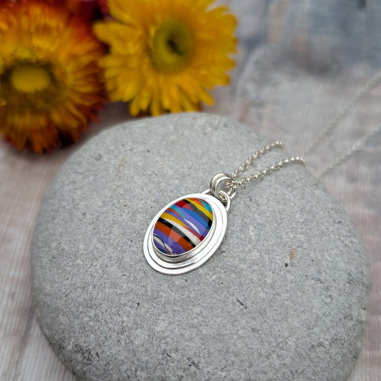 Handmade Surfite necklace displayed on a smooth stone with dried flowers in the background, showing the vibrant colours and layered detail of the pendant.