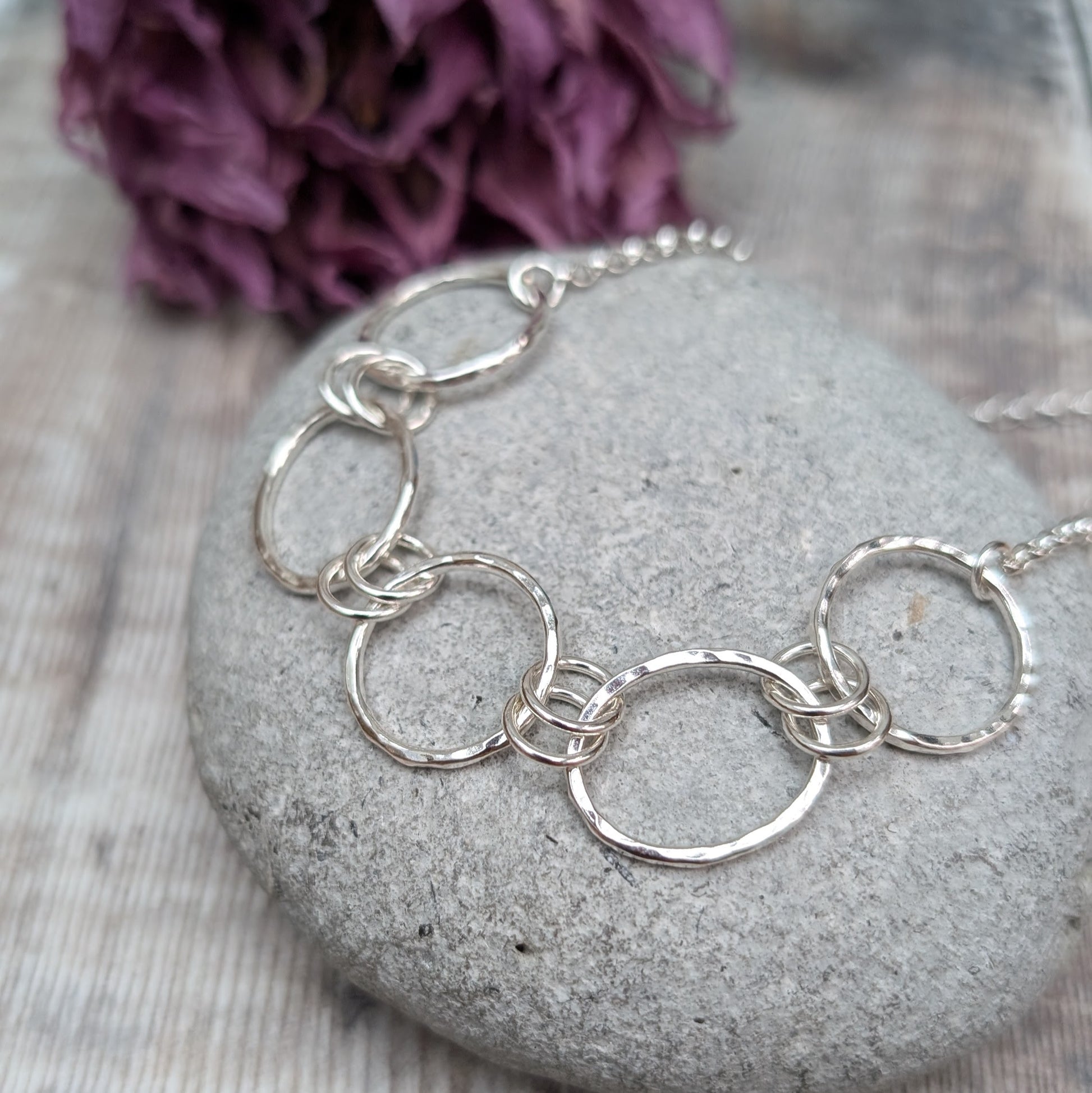 Five open silver circles with hammered finish linked with each other via two small silver circles in a repeating pattern. Each circle at each end of the pattern is attached to a silver chain.