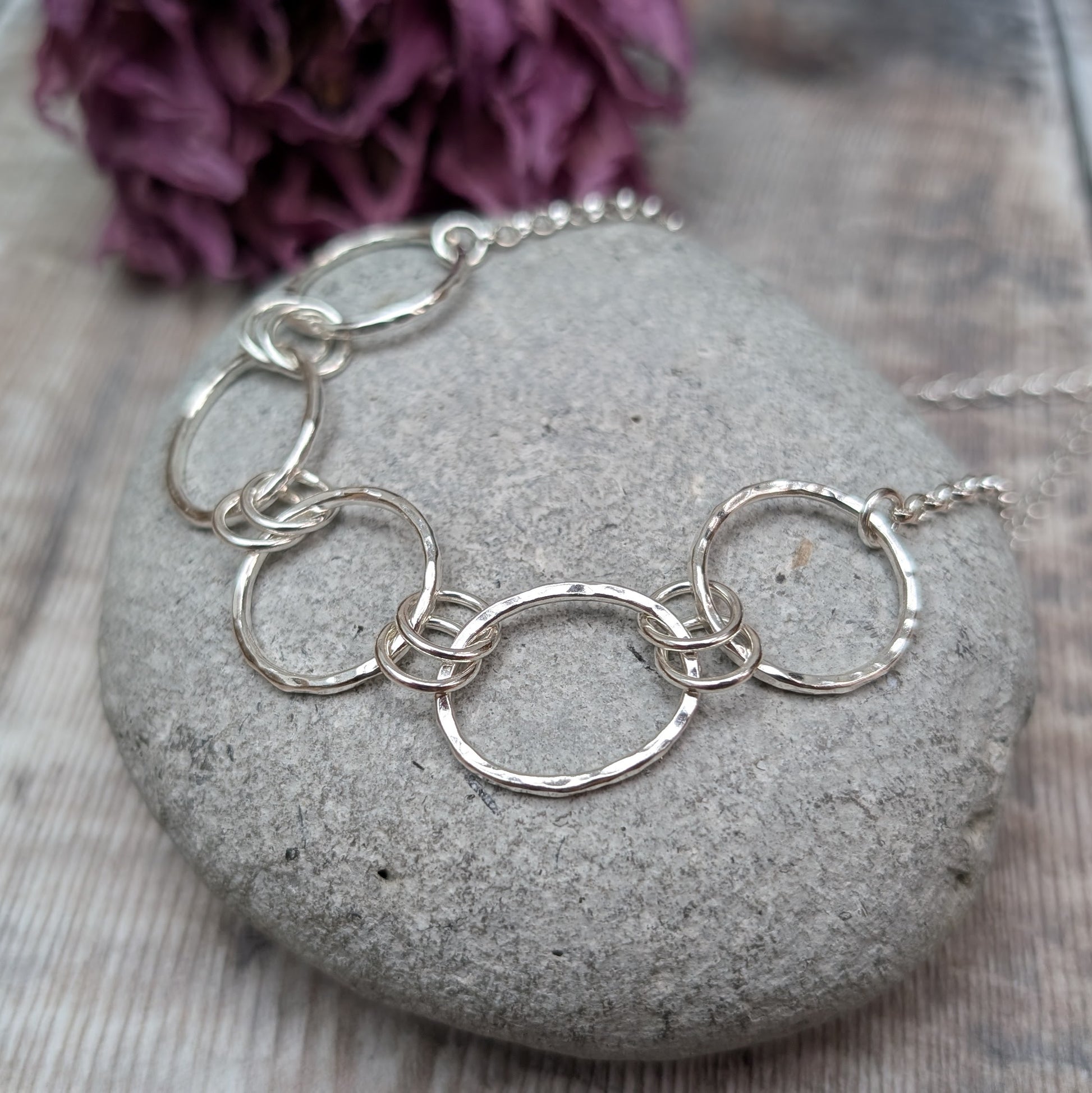 Five open silver circles with hammered finish linked with each other via two small silver circles in a repeating pattern. Each circle at each end of the pattern is attached to a silver chain.