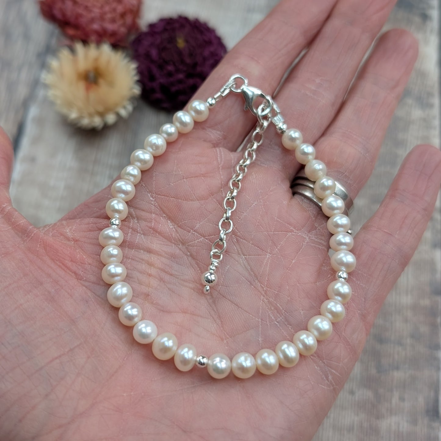 Handmade pearl bracelet with silver details, resting in an open hand to show scale and finish.