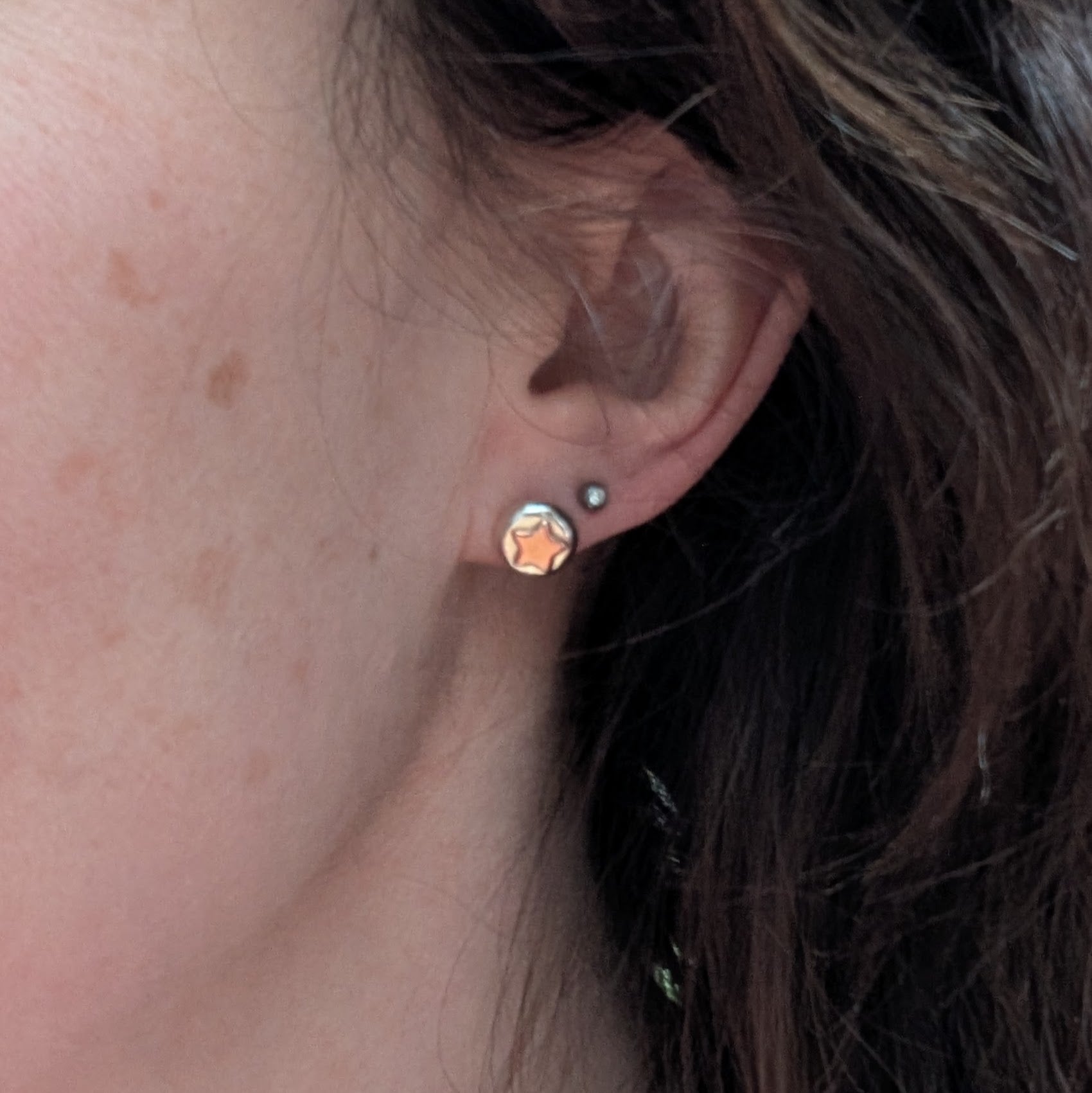 Stud Earrings Being Worn
Close-up of a person wearing small sterling silver and copper star stud earrings. The silver pebbles have an organic, melted shape, and the copper stars catch the light. Minimalist, mixed-metal jewellery, perfect for everyday wear. Handmade in the UK.