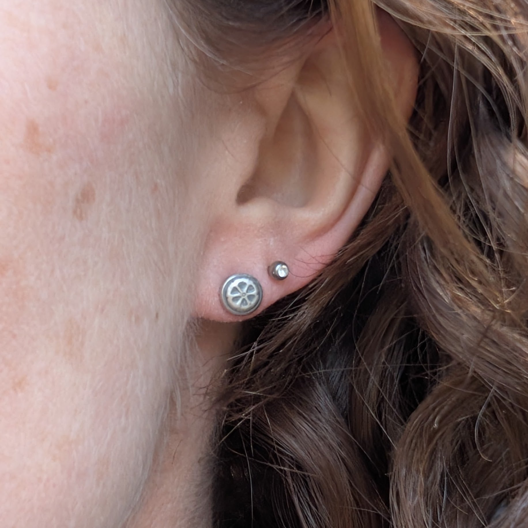 Close-up of a person wearing one of the silver flower stud earrings, paired with a small gemstone stud.