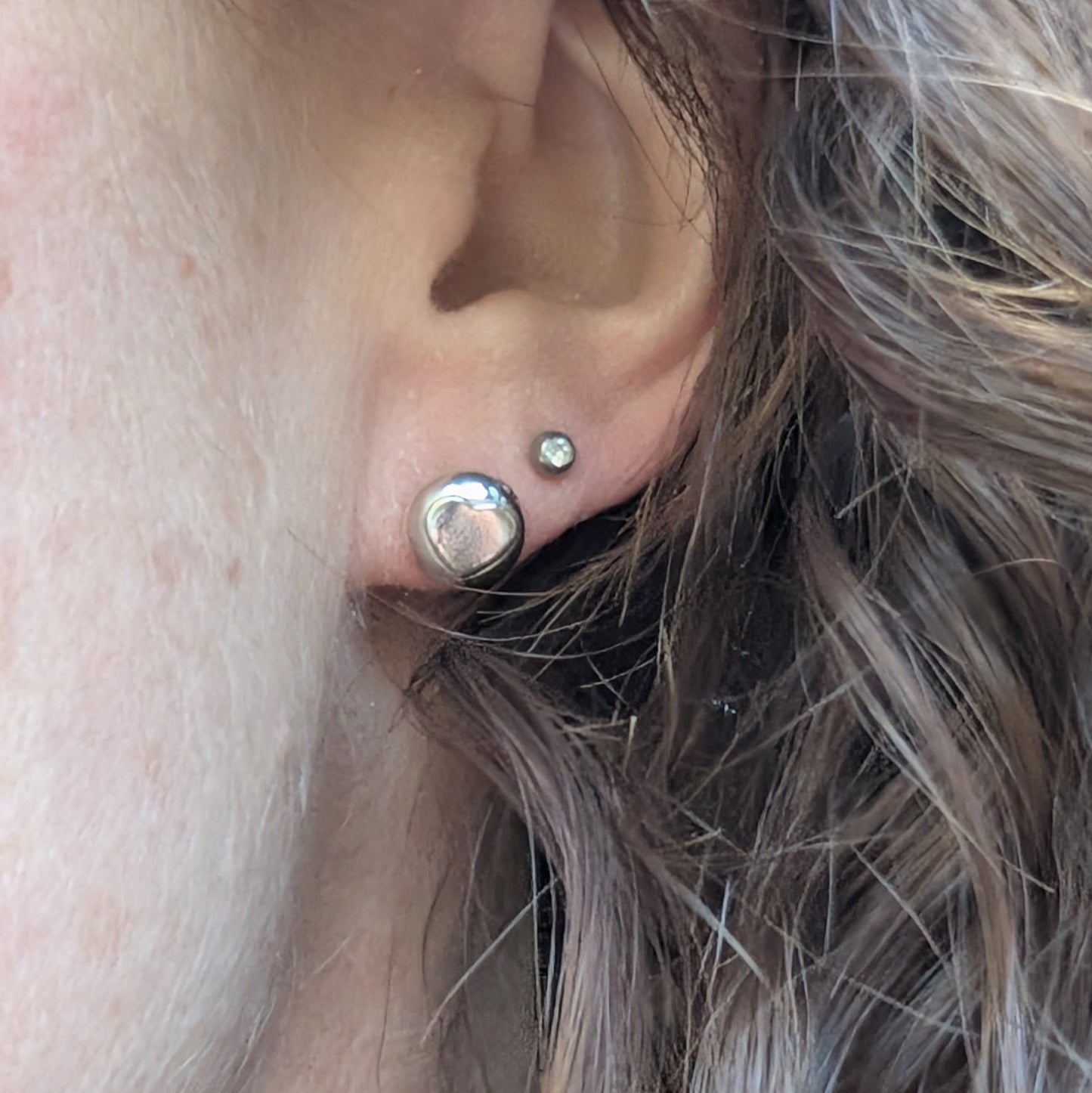 A close-up of a person wearing one of the silver heart stud earrings, showing its size and polished finish.
