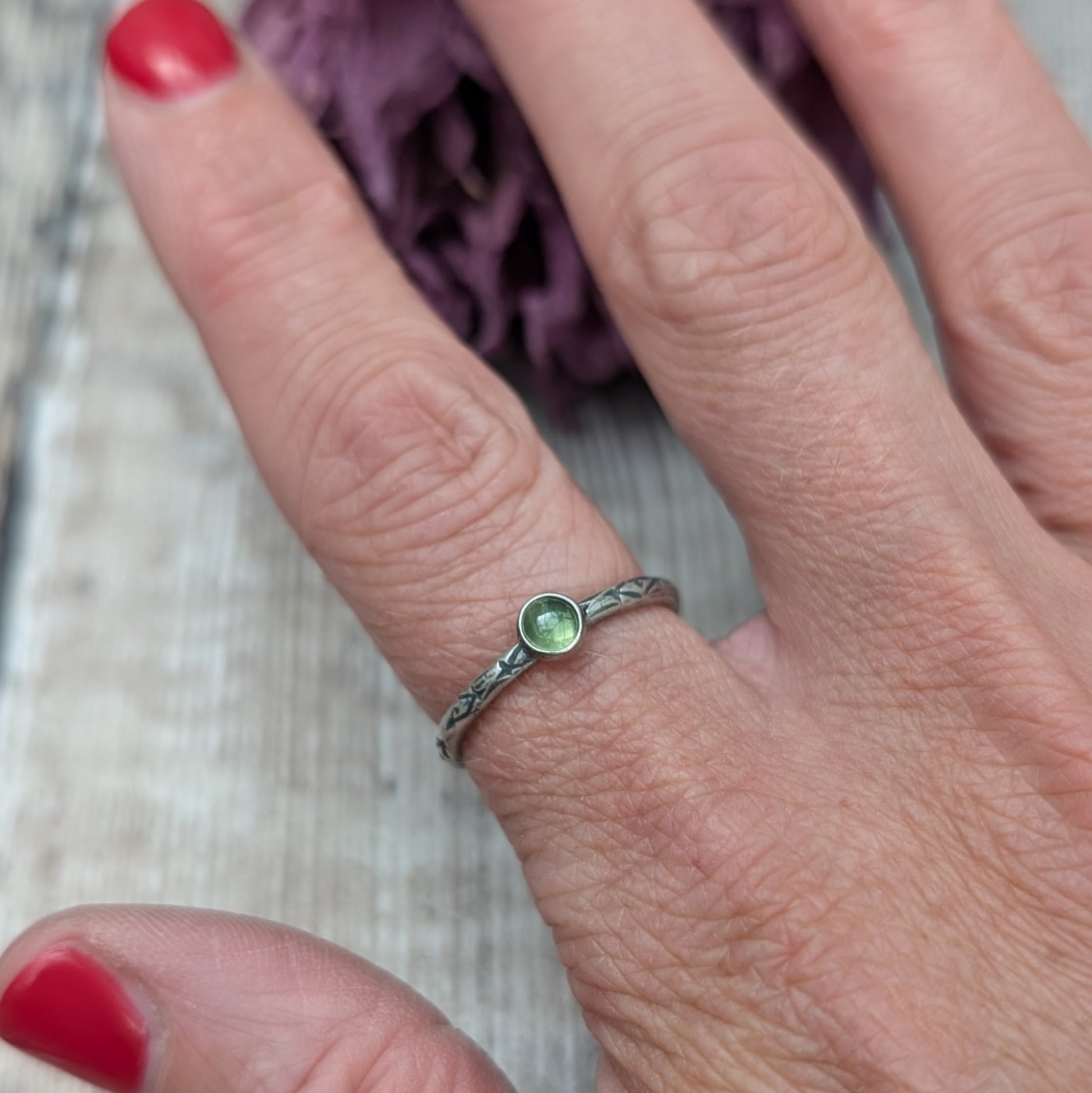 Slim silver band with cross stamped pattern. A green peridot round stone is mounted on the band in an oxidised sterling silver bezel. Rings can be stacked above or below this piece.