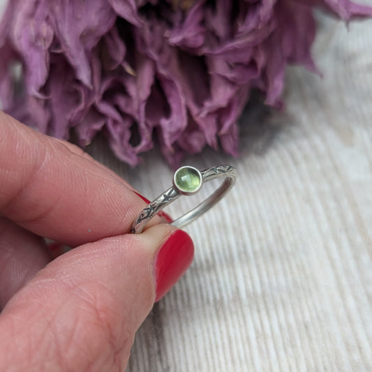 Slim silver band with cross stamped pattern. A green peridot round stone is mounted on the band in an oxidised sterling silver bezel. Rings can be stacked above or below this piece.