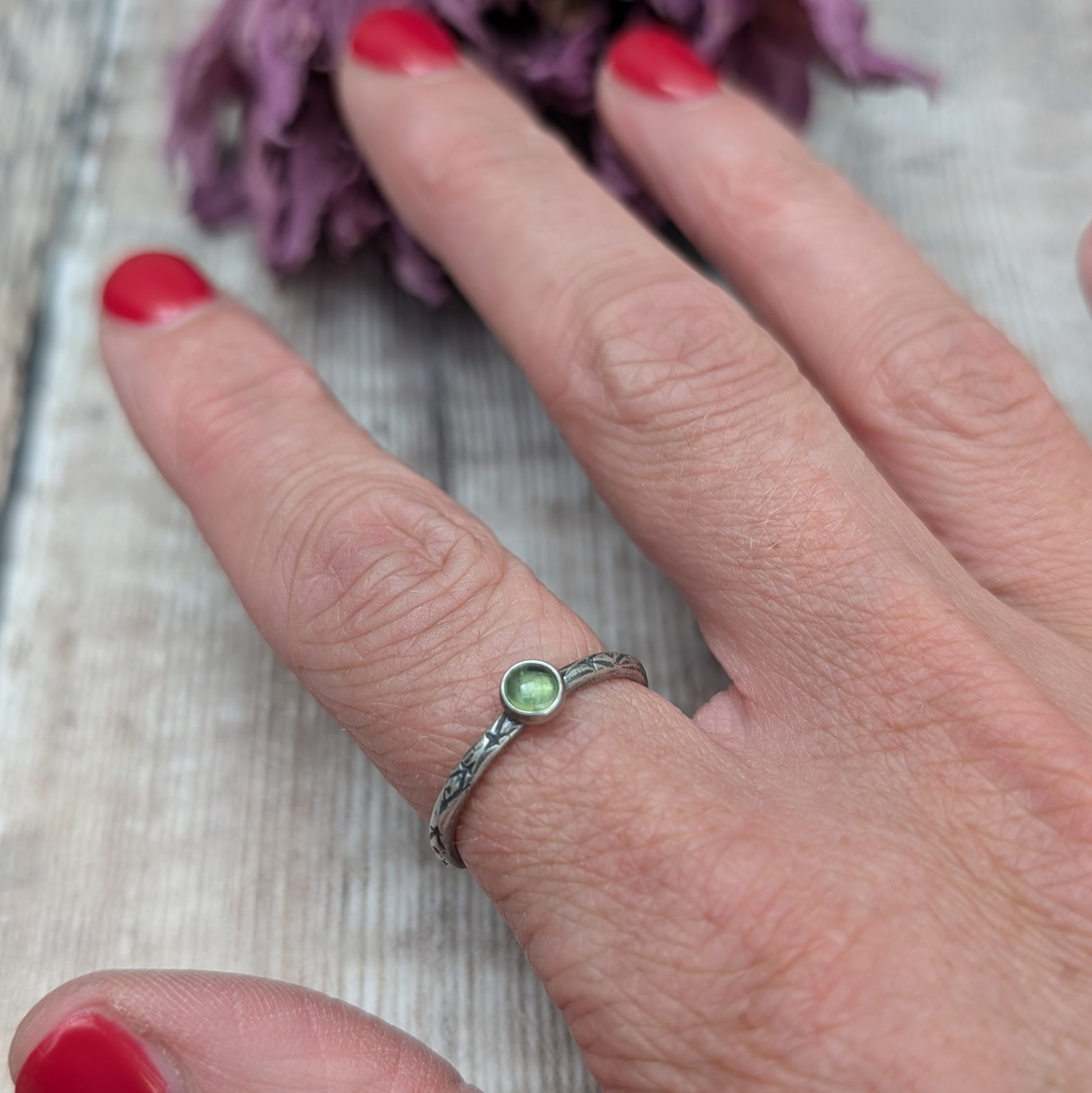 Slim silver band with cross stamped pattern. A green peridot round stone is mounted on the band in an oxidised sterling silver bezel. Rings can be stacked above or below this piece.