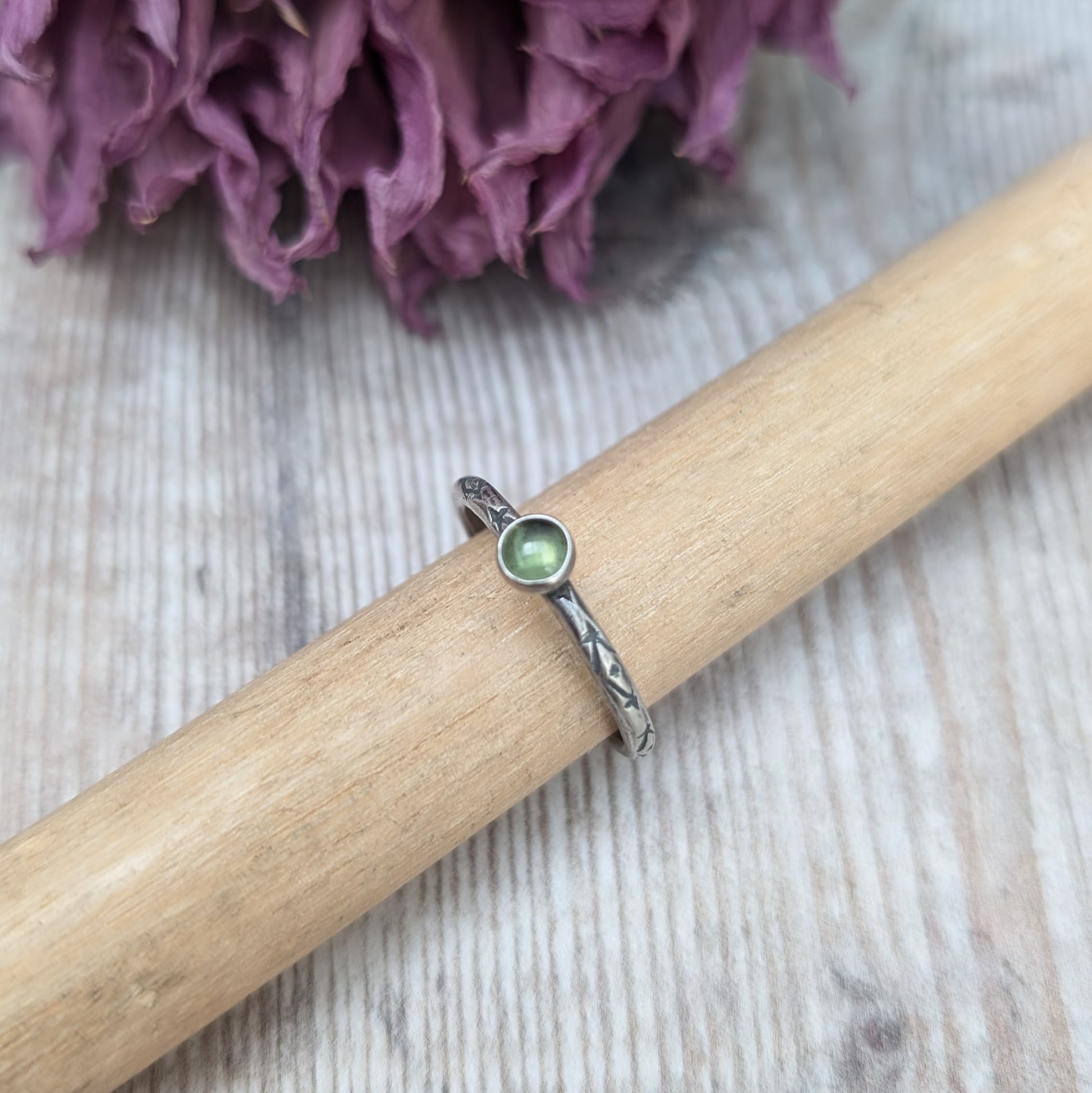 Slim silver band with cross stamped pattern. A green peridot round stone is mounted on the band in an oxidised sterling silver bezel. Rings can be stacked above or below this piece.