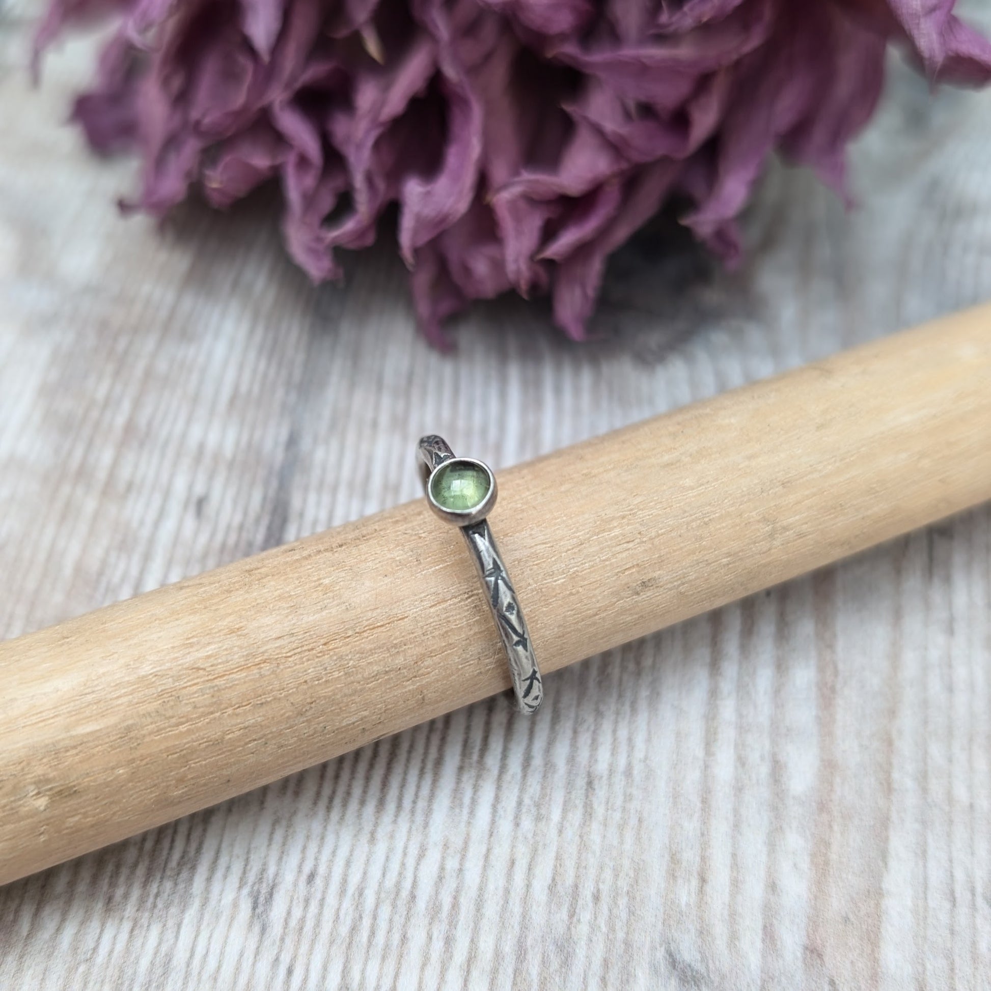 Slim silver band with cross stamped pattern. A green peridot round stone is mounted on the band in an oxidised sterling silver bezel. Rings can be stacked above or below this piece.