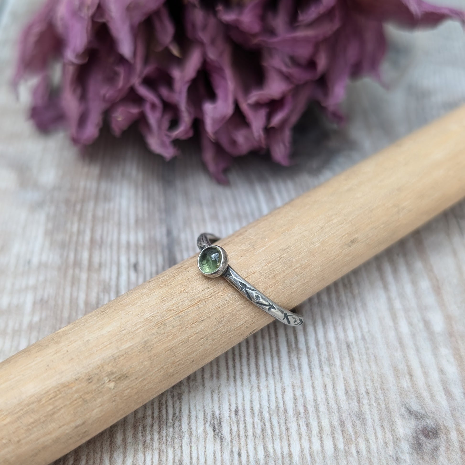 Slim silver band with cross stamped pattern. A green peridot round stone is mounted on the band in an oxidised sterling silver bezel. Rings can be stacked above or below this piece.