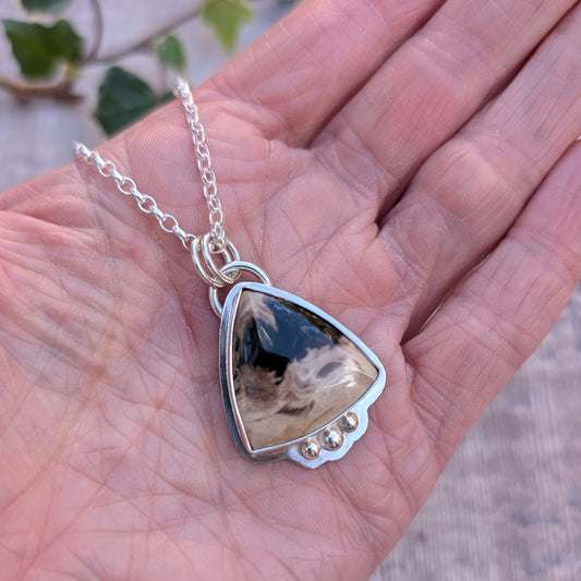 Petrified Palm Wood Statement Gemstone Necklace handmade from recycled sterling silver, featuring a triangular black and cream gemstone with three silver ball details, photographed in the palm of a hand.