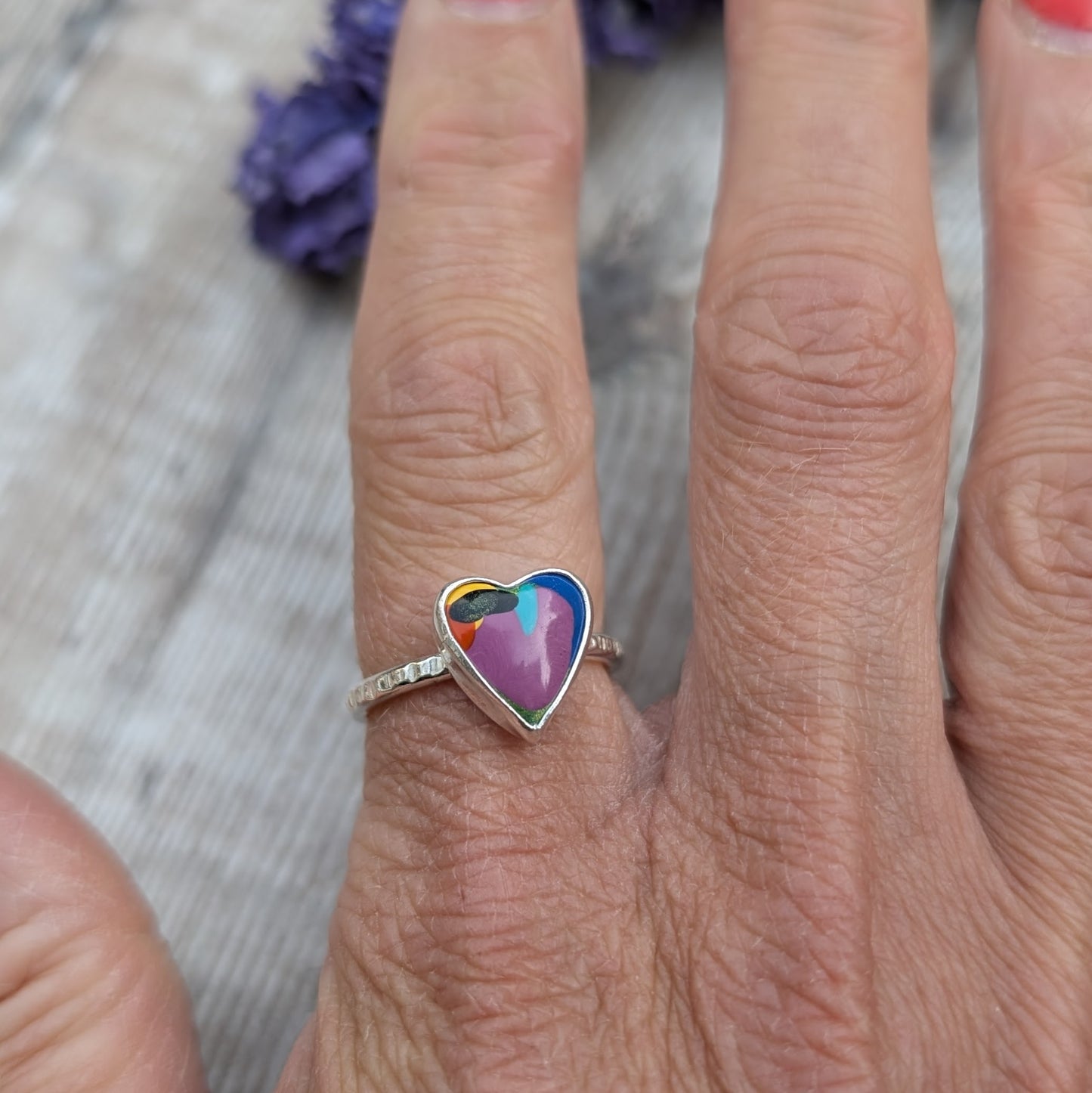 Hand wearing a heart-shaped Surfite ring in recycled sterling silver, showing the colourful resin stone against the skin.