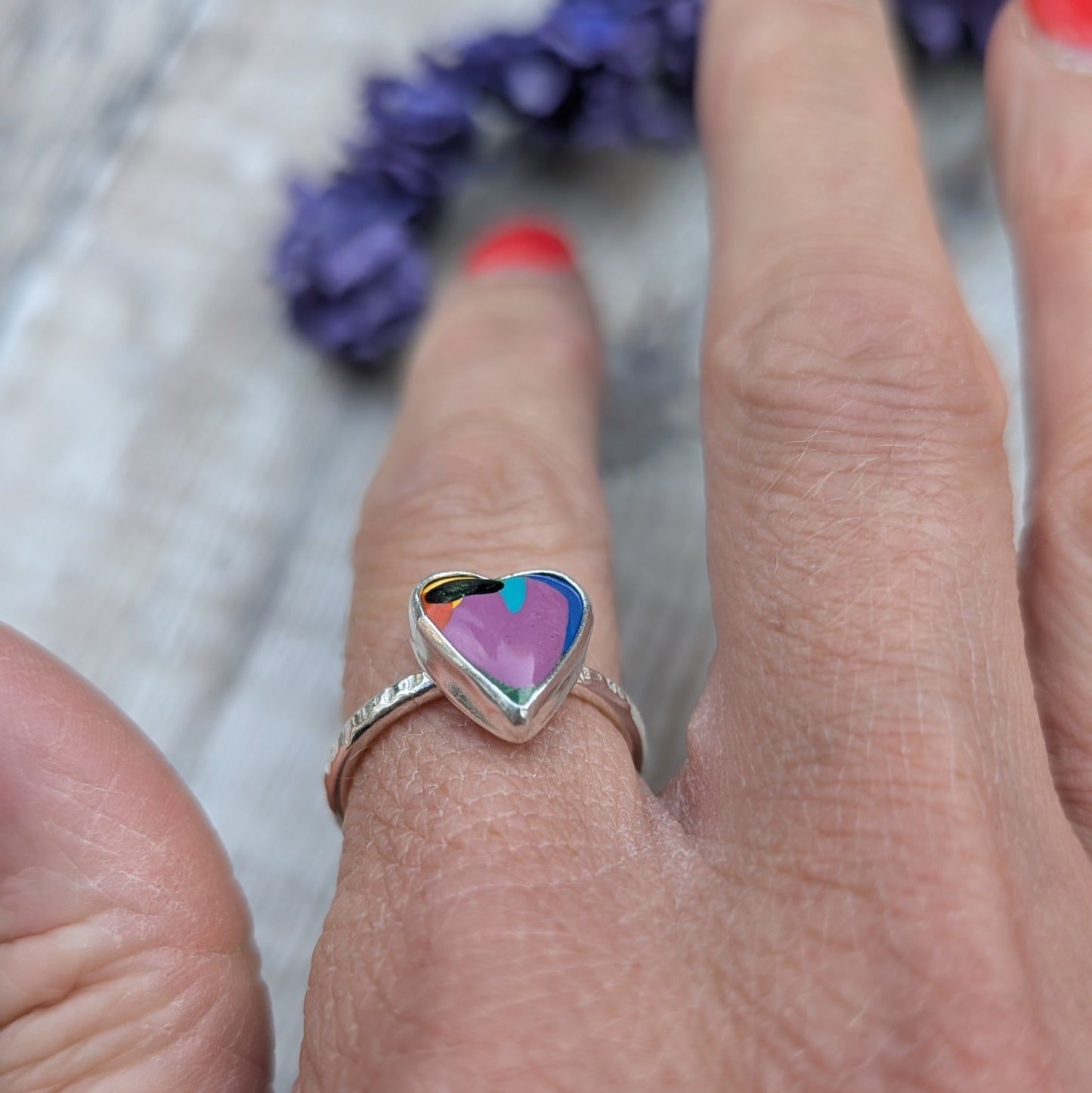 Hand wearing a heart-shaped Surfite ring in recycled sterling silver, showing the colourful resin stone against the skin.