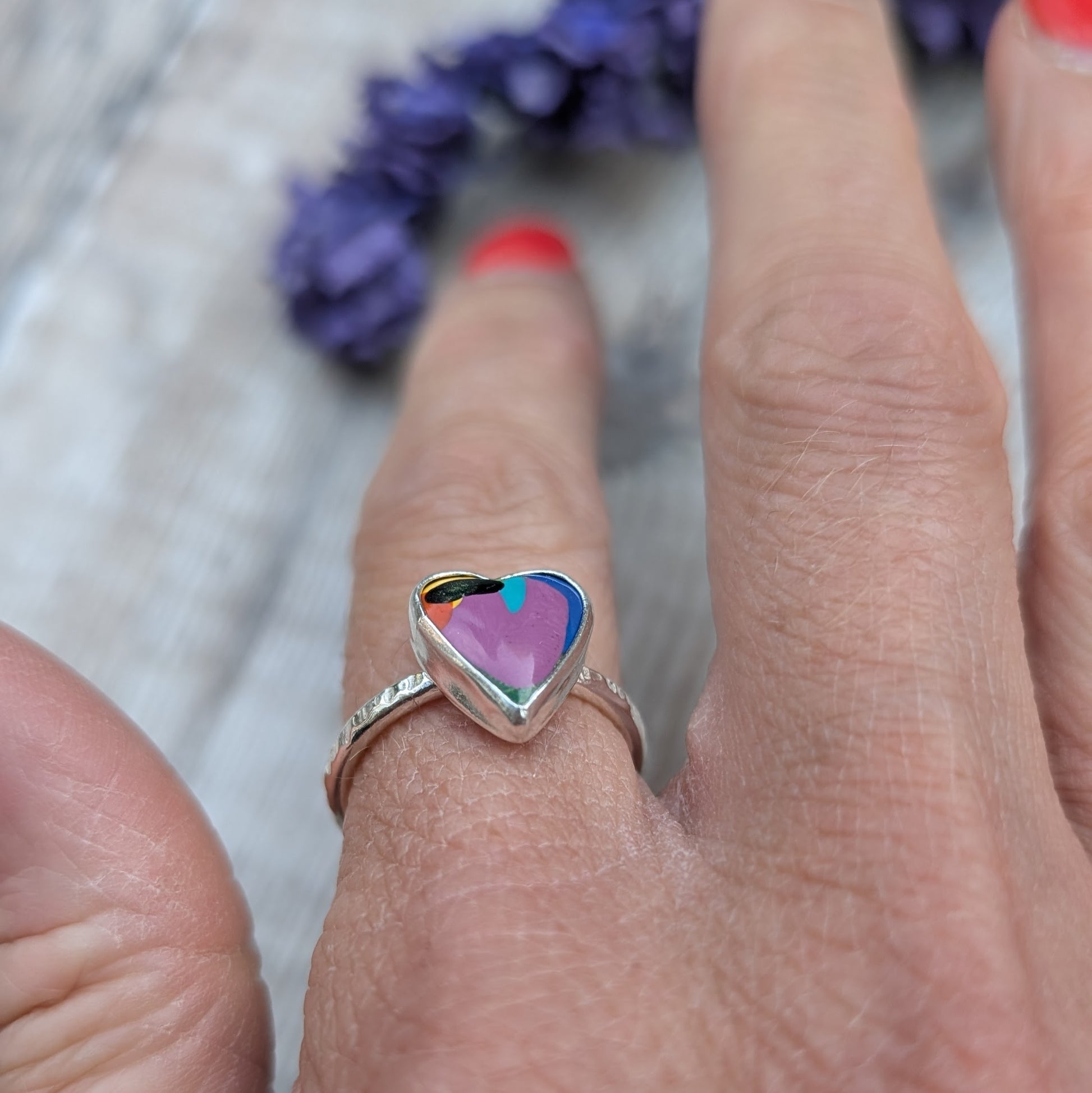 Hand wearing a heart-shaped Surfite ring in recycled sterling silver, showing the colourful resin stone against the skin.