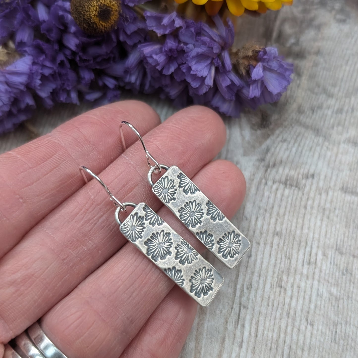 Each earring is a long rectangle stamped with multiple daisy shapes. The daisy pattern stands out after oxidisation. Rectangle pendant is suspended from silver earring wire.