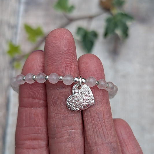 Close up of the rose quartz and silver floral heart charm bracelet showing the handmade recycled sterling silver heart with its detailed floral pattern and pale pink gemstone beads.