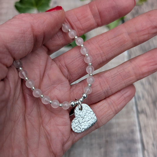 Rose Quartz and Silver Floral Heart Necklace held in a hand, showing the soft pink gemstone beads, small silver spacers and handmade silver heart charm with its textured floral design.