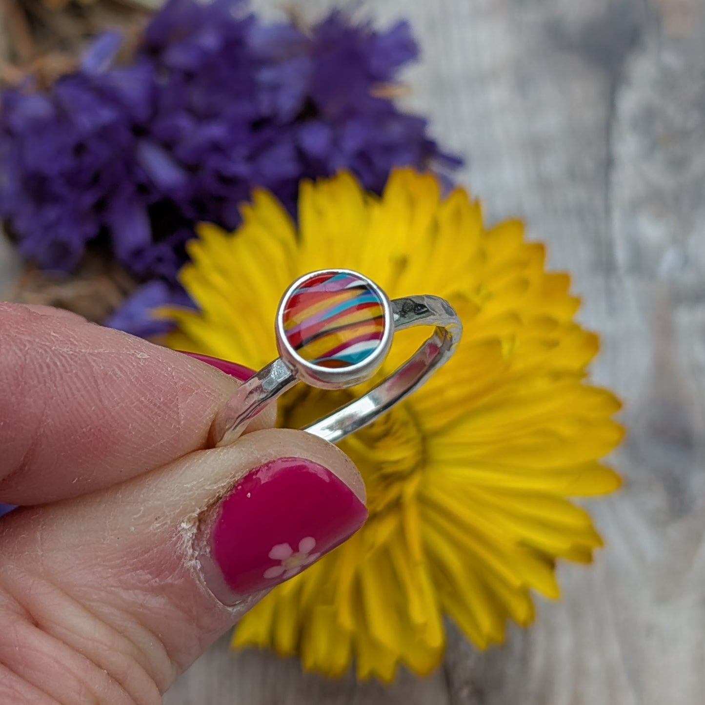 Front view of the Surfite ring held between fingers, showing the striped colours of the Surfite stone and hammered silver band.