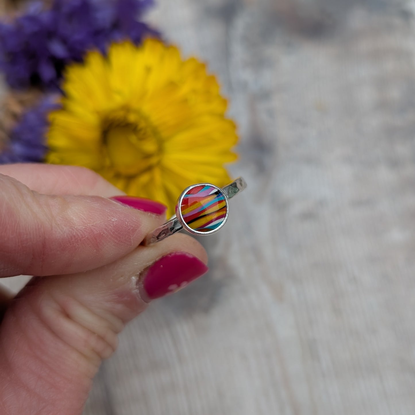 Front view of the Surfite ring held between fingers, showing the striped colours of the Surfite stone and hammered silver band.