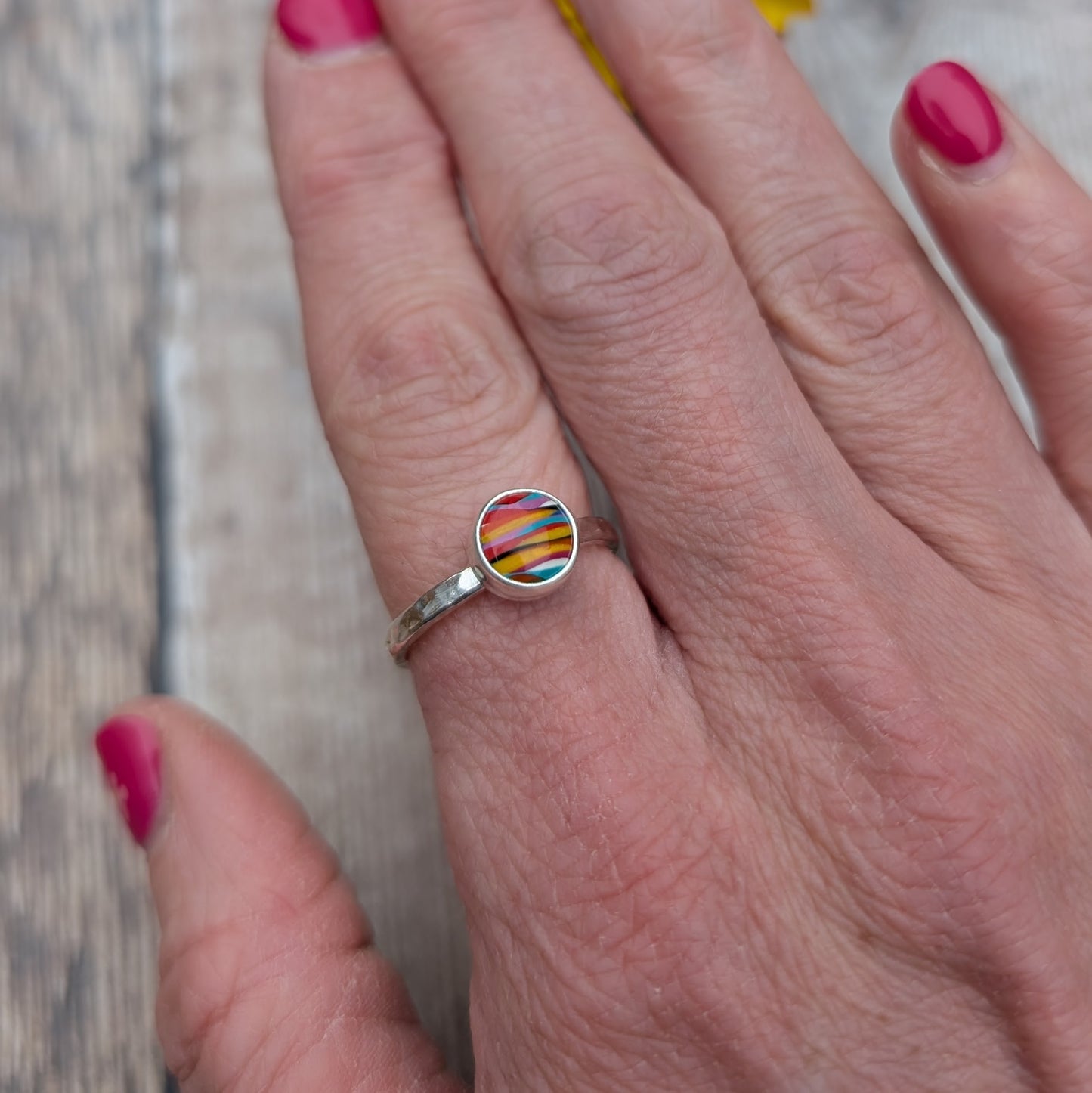 Close-up of a colourful round Surfite ring with a hammered sterling silver band, worn on a hand with pink nail polish.