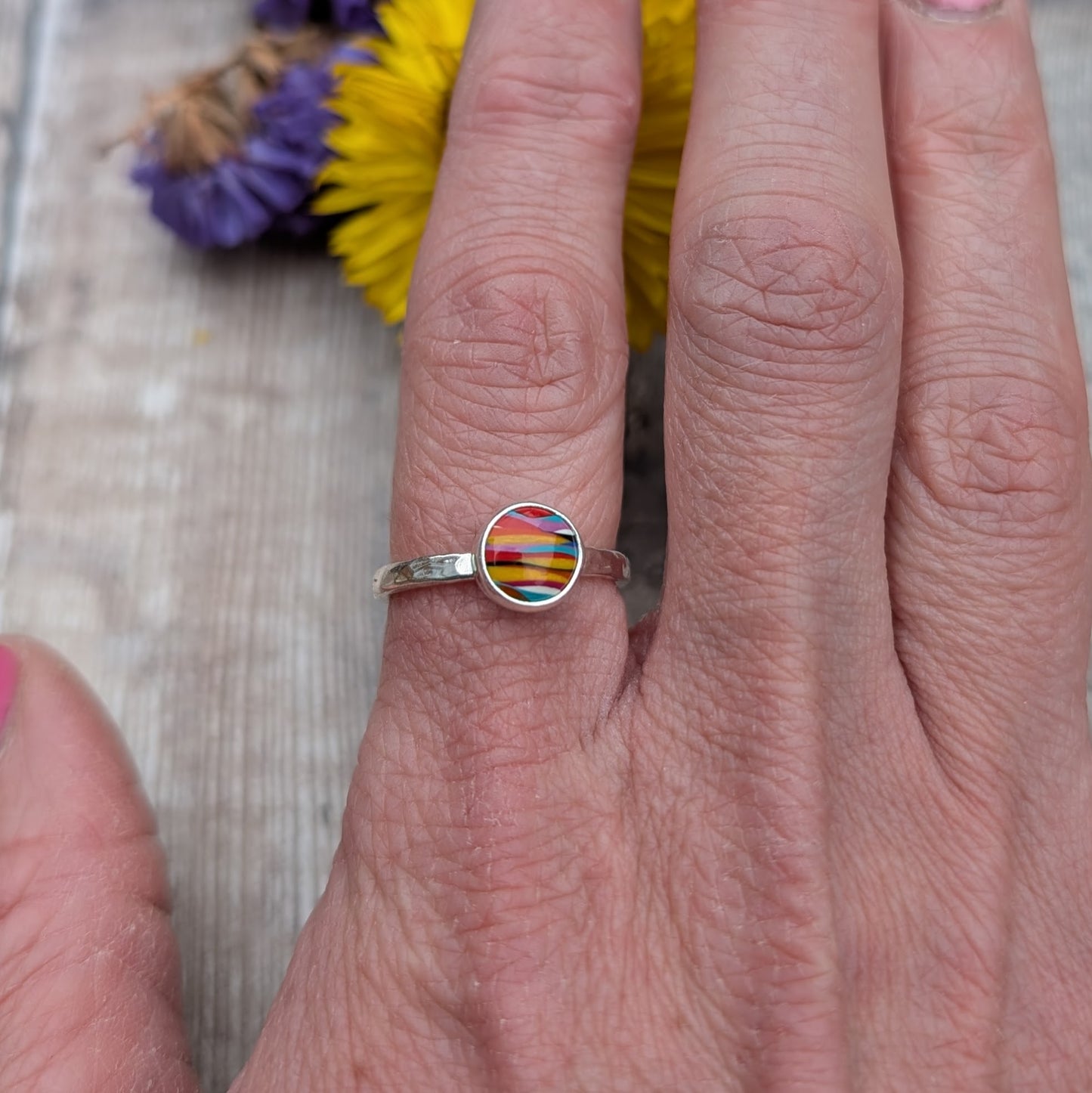 Close-up of a colourful round Surfite ring with a hammered sterling silver band, worn on a hand with pink nail polish.