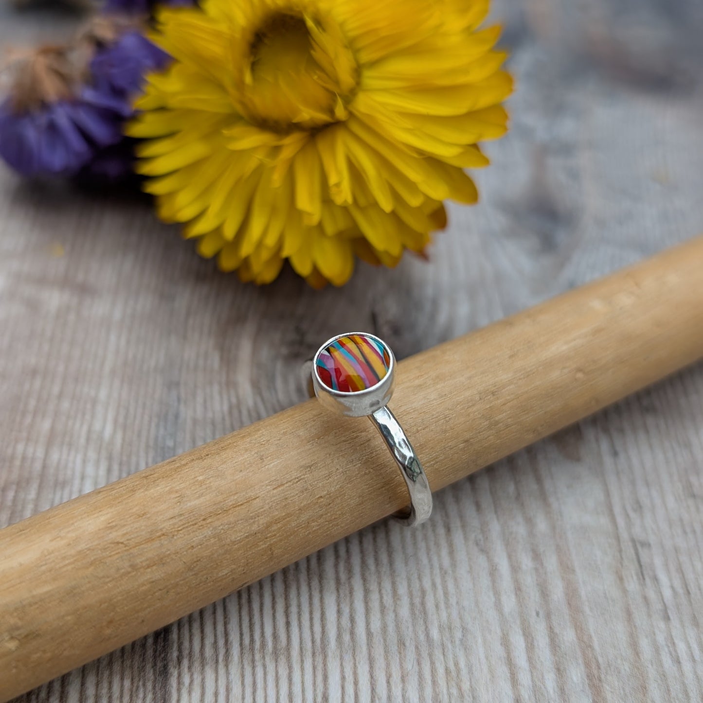 Handmade Surfite ring displayed on a wooden ring mandrel with a yellow flower in the background.