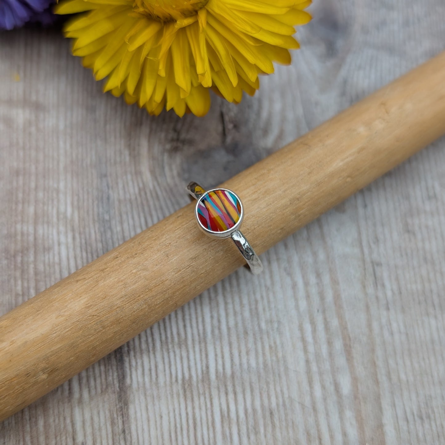 Handmade Surfite ring displayed on a wooden ring mandrel with a yellow flower in the background.