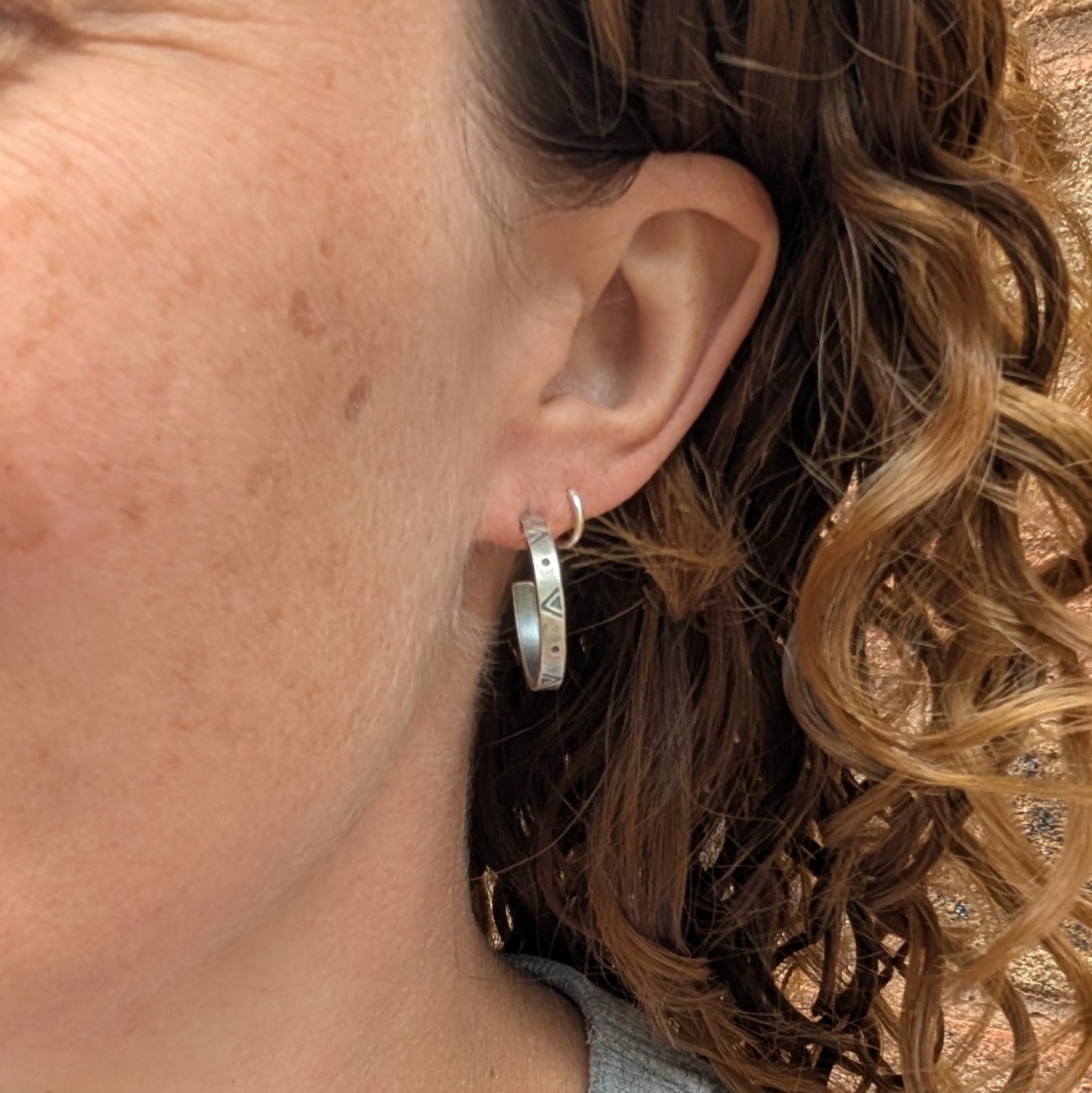 The silver geometric hoop earrings being worn in the lobe, paired with a small silver hoop in the second piercing.