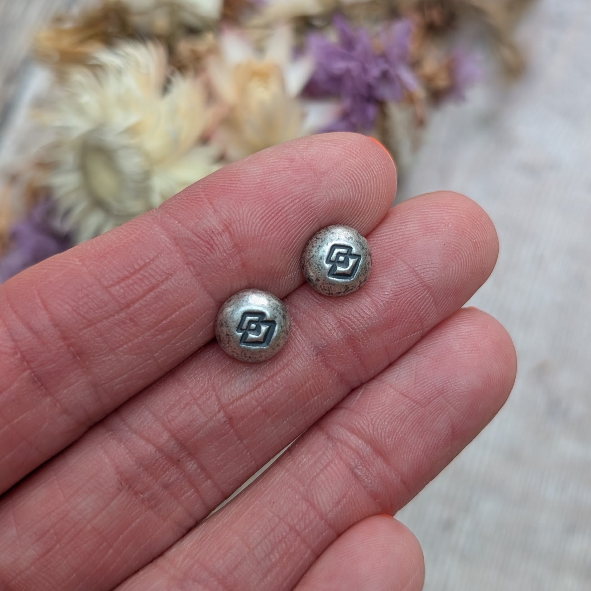 The Silver Geometric Pebble Studs resting on a person's fingertips, showing the stamped geometric pattern clearly.