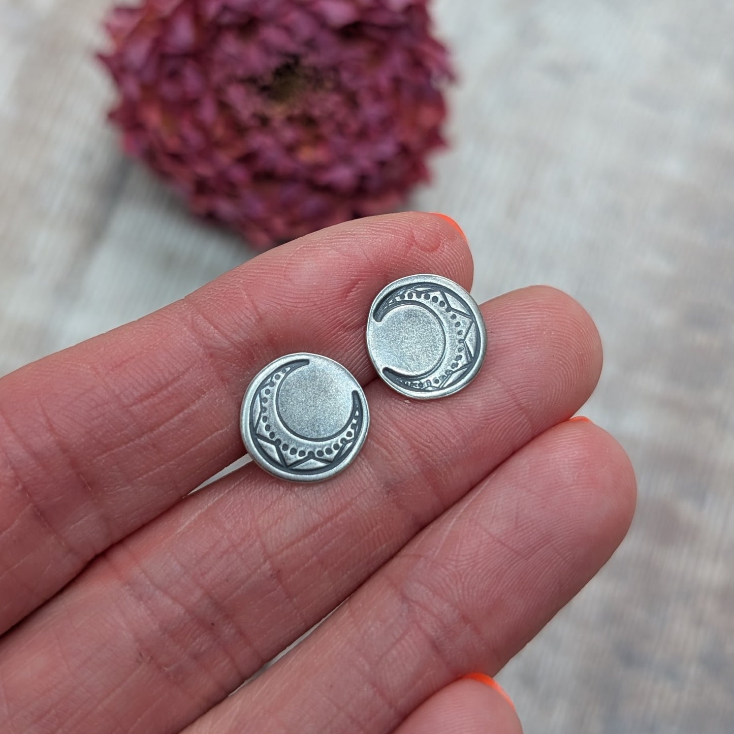 Silver large moon disc stud earrings resting on fingertips with engraved moon and dot detailing.