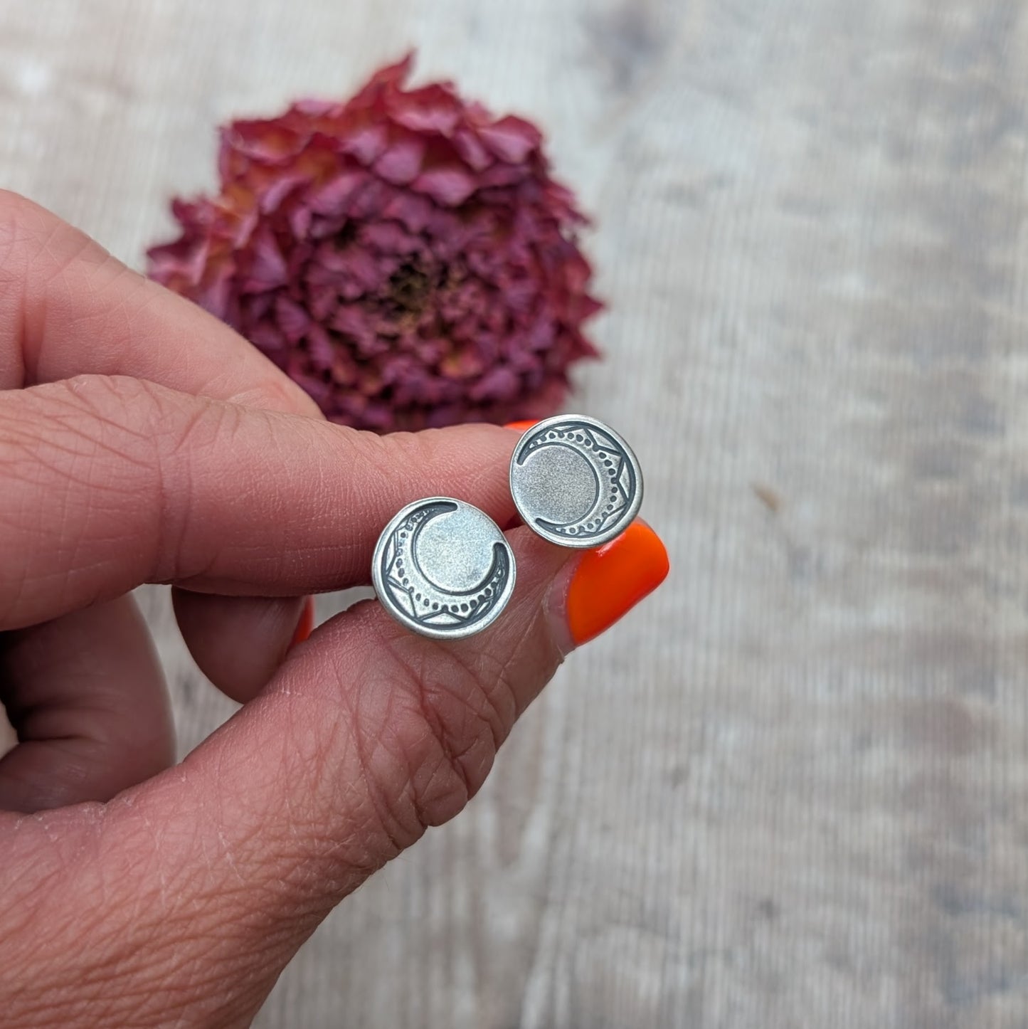 Silver large moon disc earrings held between fingers with dried flower background.