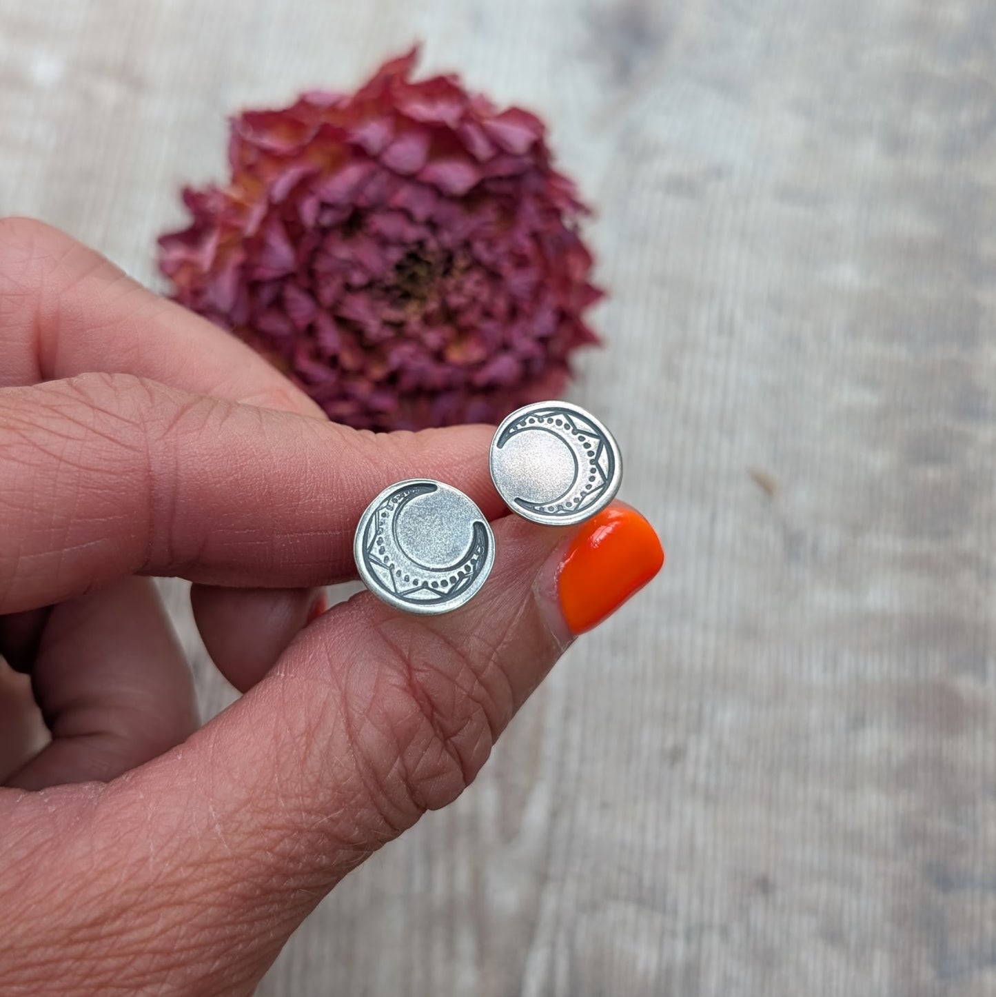 Silver large moon disc earrings held between fingers with dried flower background.