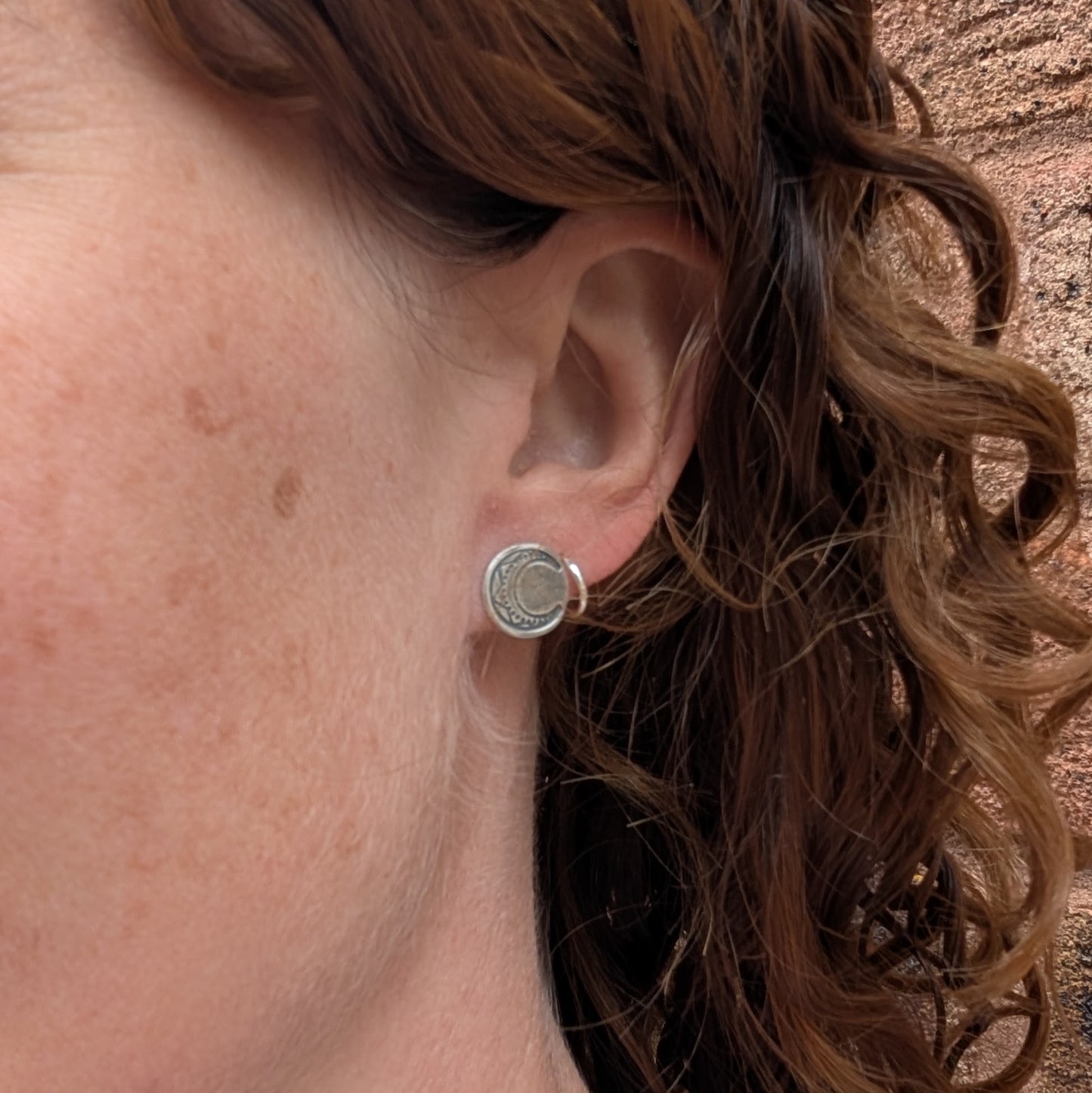 Silver moon disc stud earrings worn on ear, showing size and fit.