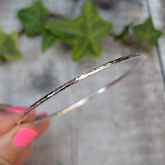 Close up side view of a Silver 2mm Hammered Round Bangle being held, showing the hammered texture along the 2mm silver wire.