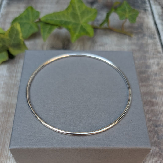 Silver 2mm Smooth Round Bangle handmade from recycled Sterling Silver, displayed on a grey jewellery box with green ivy in the background.