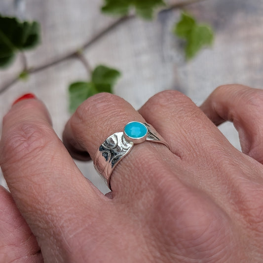 Silver oval patterned Amazonite wide band ring worn on a hand, showing the bright blue oval Amazonite stone and textured silver band.