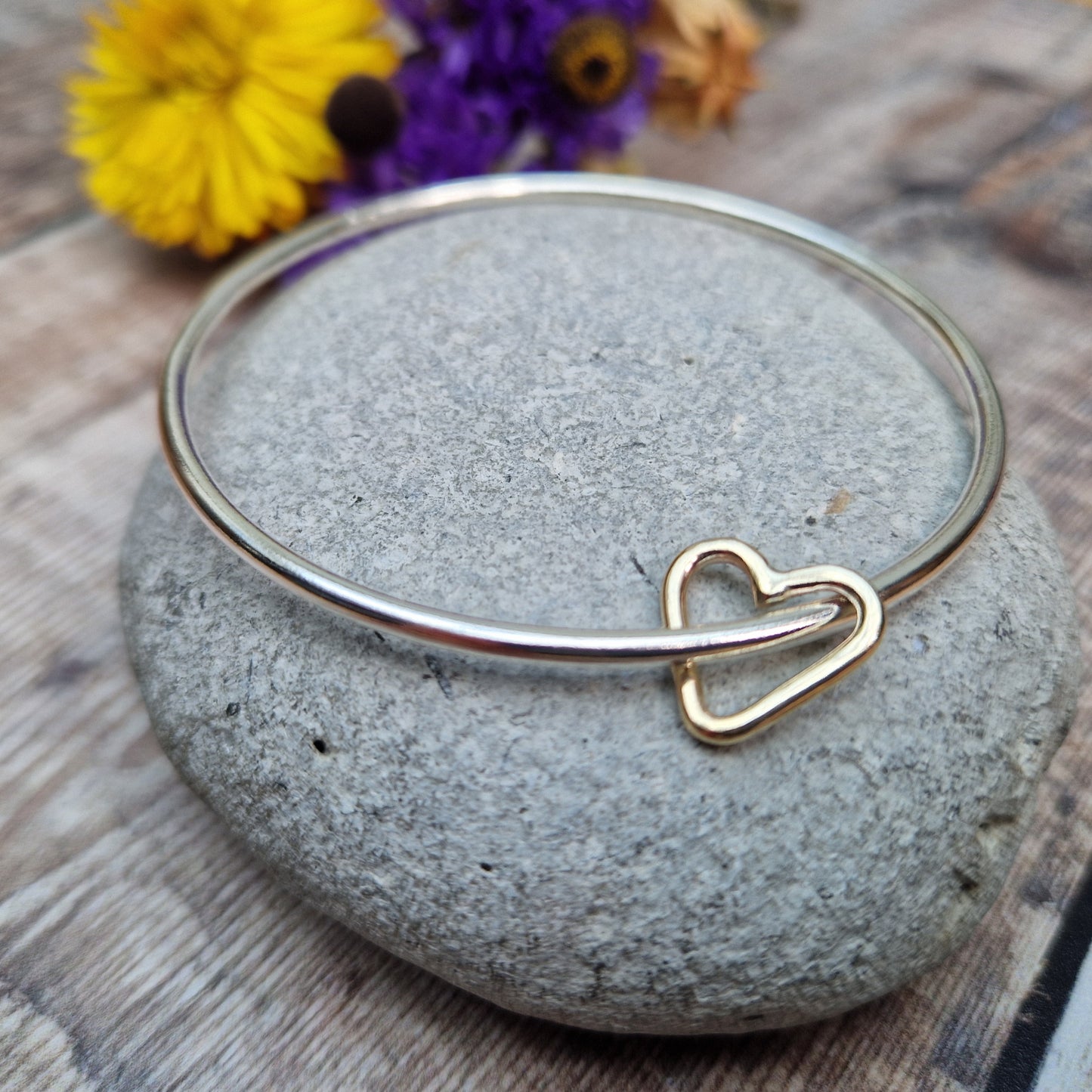 Sterling Silver bangle passes through a smaller a 9ct Gold open heart shape. Heart moves independently around the bangle.