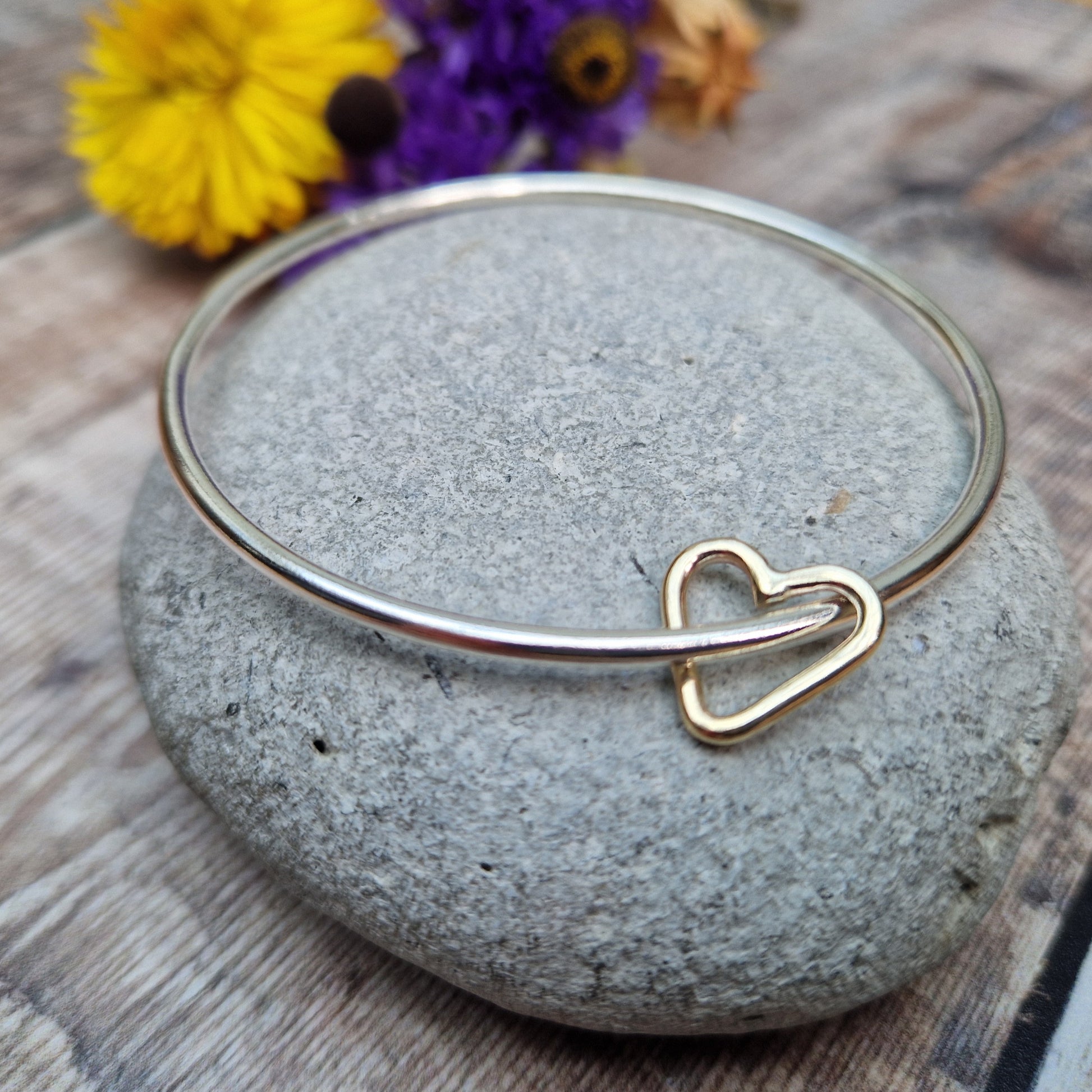 Sterling Silver bangle passes through a smaller a 9ct Gold open heart shape. Heart moves independently around the bangle.