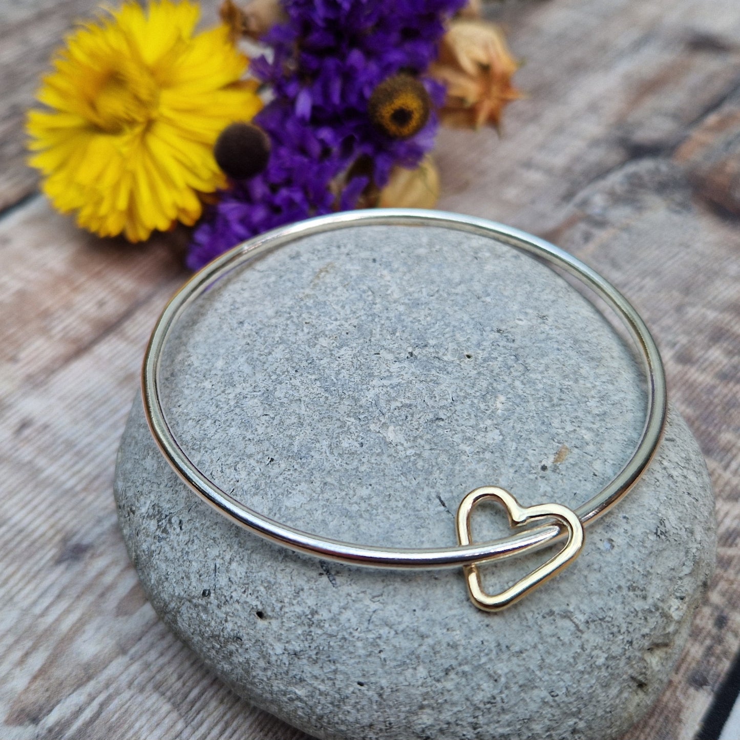 Sterling Silver bangle passes through a smaller a 9ct Gold open heart shape. Heart moves independently around the bangle.