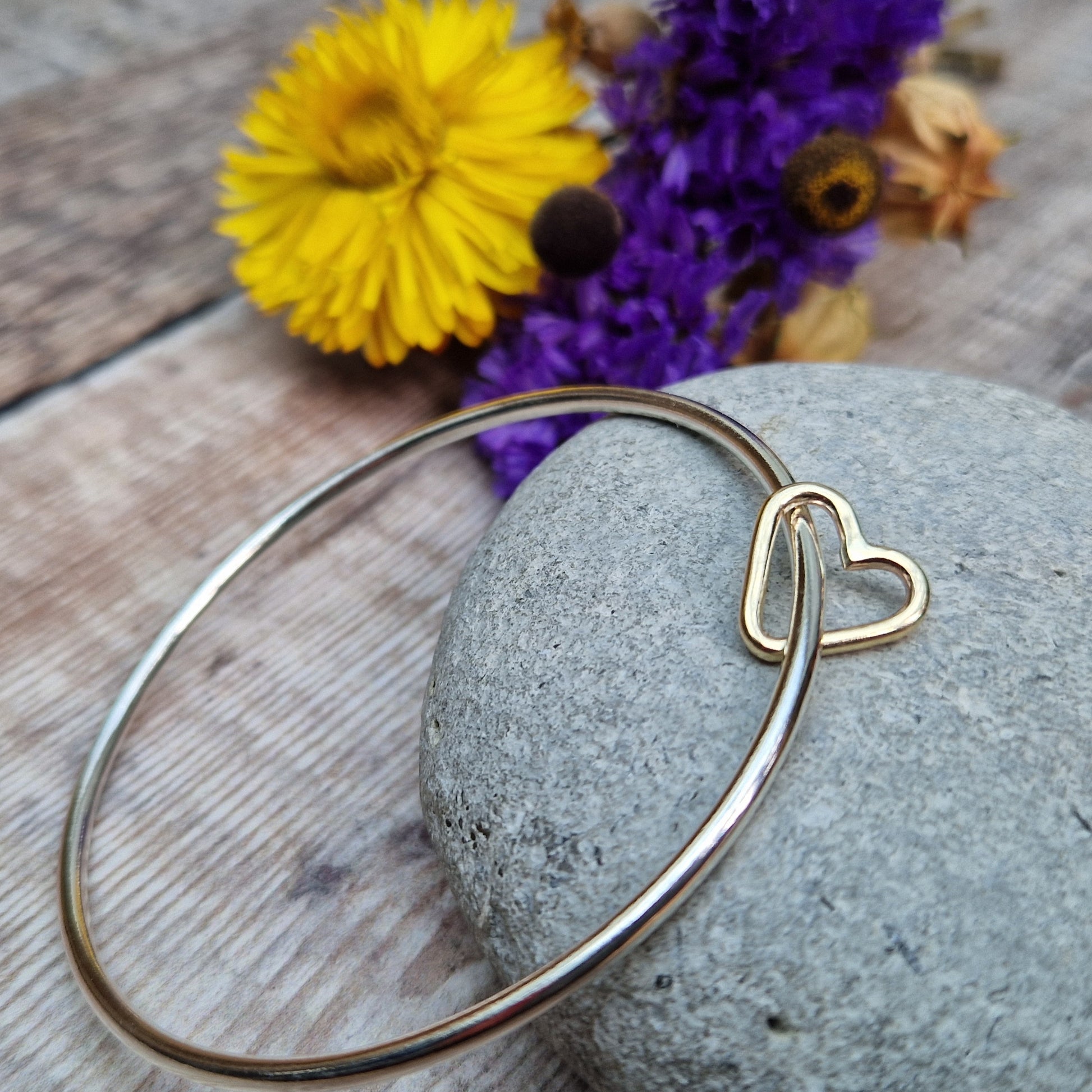 Sterling Silver bangle passes through a smaller a 9ct Gold open heart shape. Heart moves independently around the bangle.