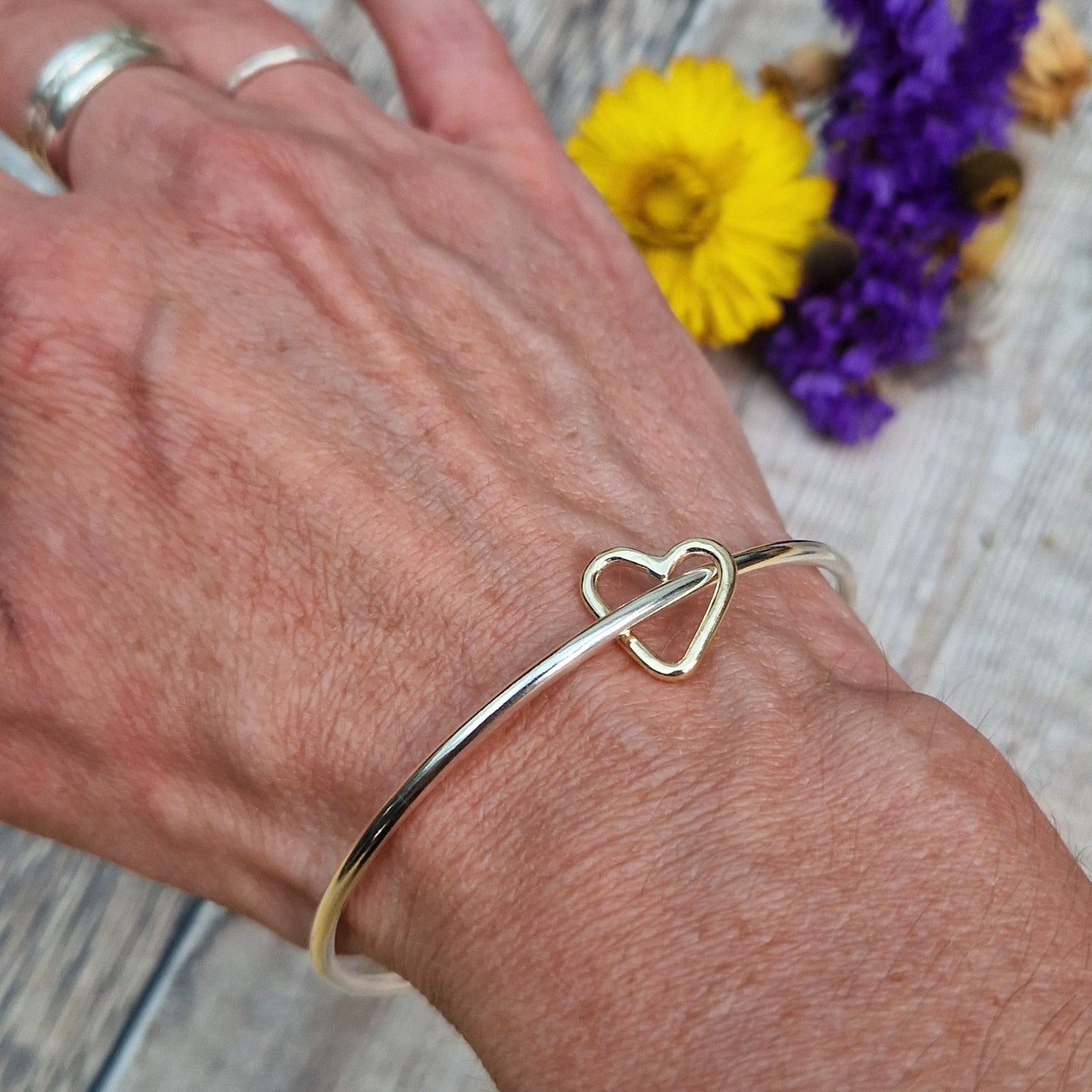 Sterling Silver bangle passes through a smaller a 9ct Gold open heart shape. Heart moves independently around the bangle.