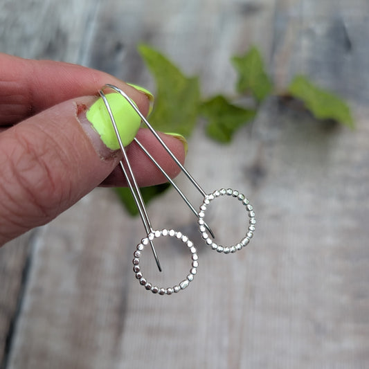 Silver beaded circle long earrings held by hand, showing the long ear wires and textured beaded silver circles.