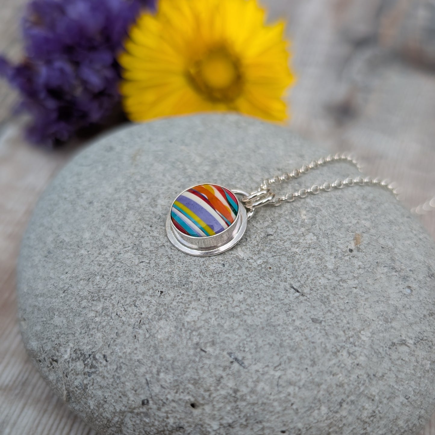 Silver Colourful Small Round Surfite Necklace displayed on a stone with flowers softly blurred behind